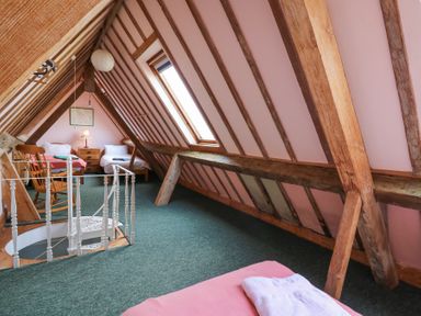An attic bedroom with exposed wooden beams two single beds a rocking chair a small chest of drawers and a skylight window at Plas Pontfaen near Fishguard and Newport Pembrokeshire
