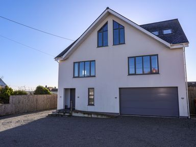 A modern two-story house with a garage and multiple windows in a gravel driveway at Plas Gwylan in Rhosneigr