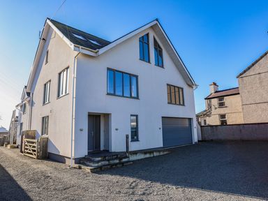 Exterior view of a white multi-story house with several windows and a garage at Plas Gwylan in Rhosneigr