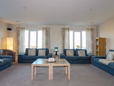A living room with blue sofas a wooden coffee table and a lamp at Plas Gwylan in Rhosneigr