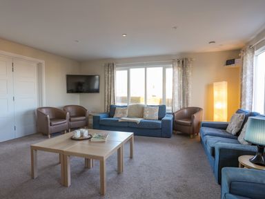 A living room with blue sofas brown armchairs a wooden coffee table and a wall-mounted TV at Plas Gwylan in Rhosneigr