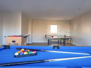 A game room with a blue pool table with balls and cues a foosball table and a ping pong table at Plas Gwylan in Rhosneigr