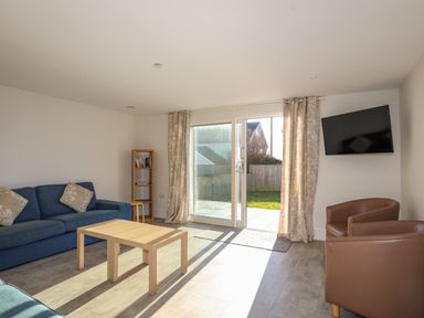 A living room with a blue sofa two brown armchairs a wooden coffee table a small bookshelf and a wall-mounted TV at Plas Gwylan in Rhosneigr