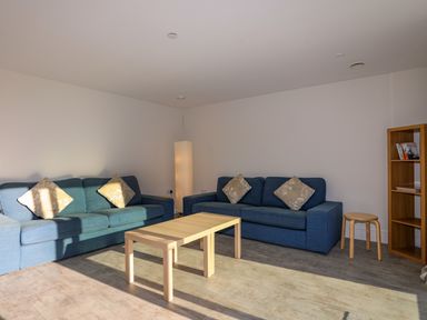 A living room with two blue sofas a wooden coffee table a floor lamp and a wooden shelf at Plas Gwylan in Rhosneigr