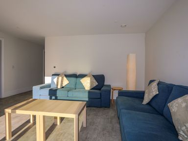A living room with blue sofas beige cushions a wooden coffee table a wooden side table and a tall floor lamp at Plas Gwylan in Rhosneigr