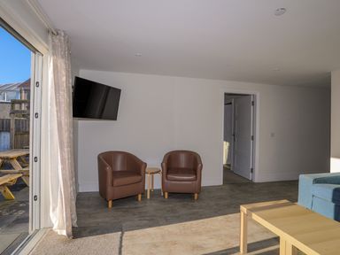 A living room with two brown chairs a small round table a wall mounted television a wooden coffee table and a blue sofa at Plas Gwylan in Rhosneigr