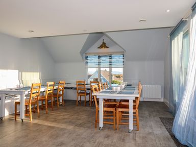 A dining area with wooden chairs around white tables and blue placemats at Plas Gwylan in Rhosneigr