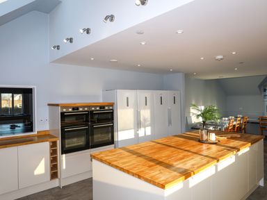 A kitchen with ovens refrigerators a wooden countertop island and a dining area with chairs at Plas Gwylan in Rhosneigr