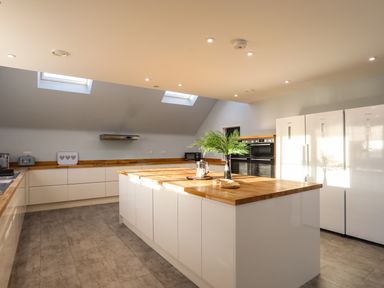 A kitchen with a large island with wooden countertop a potted plant ovens and three white refrigerators at Plas Gwylan in Rhosneigr