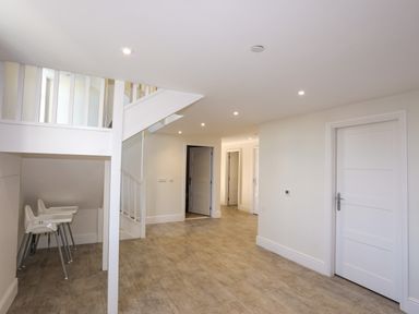 An empty room with white walls wooden floor two white high chairs under staircase and several white doors at Plas Gwylan in Rhosneigr