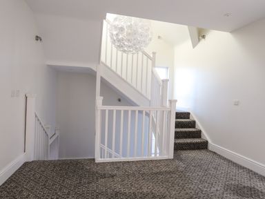 A carpeted staircase with white railings and a large round light fixture in a hallway at Plas Gwylan in Rhosneigr
