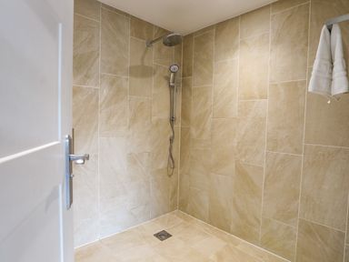 A tiled shower area with a wall-mounted showerhead and towel hanging in a bathroom at Plas Gwylan in Rhosneigr