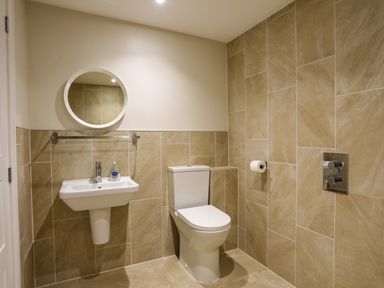 A bathroom with a toilet sink round mirror and tiled walls at Plas Gwylan in Rhosneigr