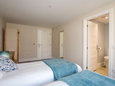 A bedroom with two beds a mirror on the wall and an open door to a bathroom at Plas Gwylan in Rhosneigr