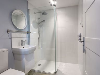 A bathroom with a shower enclosure, a pedestal sink with a mirror above it, and a toilet at Plas Gwylan in Rhosneigr