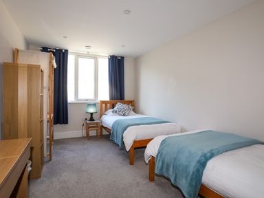 A bedroom with two single beds a window with curtains a bedside table and a lamp at Plas Gwylan in Rhosneigr