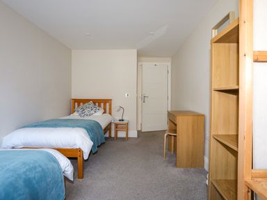 A bedroom with two single beds, a wooden desk, a chair, a nightstand with a lamp, and a wooden bookshelf at Plas Gwylan in Rhosneigr