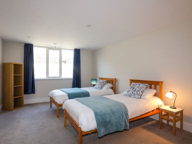 A bedroom with two single beds a small wooden shelf and blue curtains at Plas Gwylan in Rhosneigr