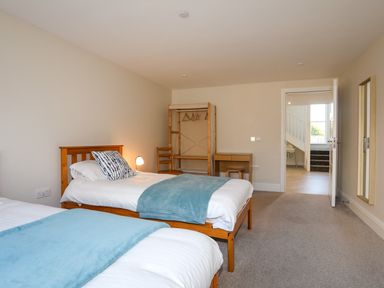A bedroom with two single beds blue blankets a wooden chair an open clothes rack and a wooden desk at Plas Gwylan in Rhosneigr