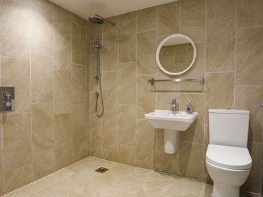 A bathroom with a wall-mounted shower head a sink with a round mirror above and a toilet at Plas Gwylan in Rhosneigr