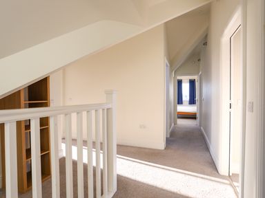 A hallway with beige carpet and white walls leading to a room with blue curtains at Plas Gwylan in Rhosneigr