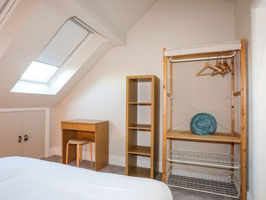 A bedroom corner with a desk and stool wooden shelves and an open clothes rack under a skylight window at Plas Gwylan in Rhosneigr