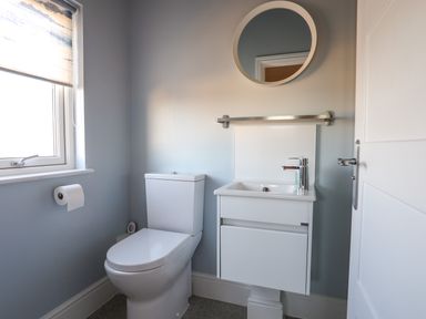 A bathroom with a toilet a sink with a faucet a round mirror and a window with a blind at Plas Gwylan in Rhosneigr