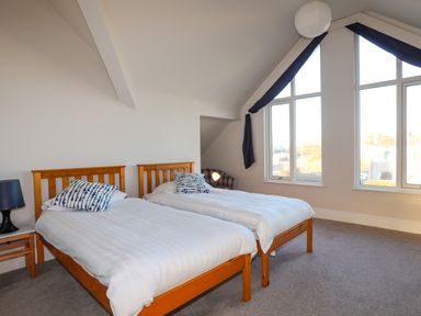 A bedroom with two wooden single beds with white bedding and blue patterned pillows near large windows at Plas Gwylan in Rhosneigr