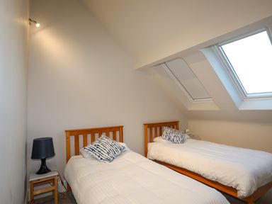 A bedroom with two single beds with white bedding and a small bedside table with a lamp under skylight windows at Plas Gwylan in Rhosneigr