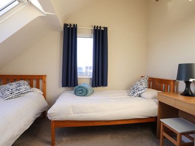 A bedroom with two single beds a desk and a window with blue curtains at Plas Gwylan in Rhosneigr