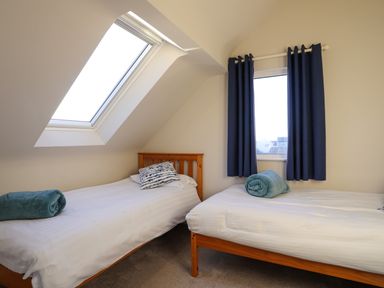 A bedroom with two single beds under a skylight and a window with blue curtains at Plas Gwylan in Rhosneigr