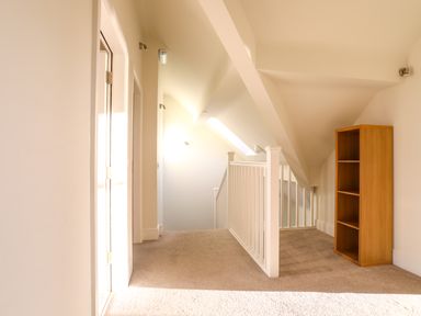 A hallway with a white railing and an empty wooden bookshelf at Plas Gwylan in Rhosneigr