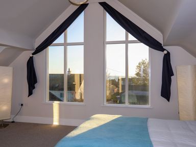 A bedroom with large triangular windows and blue curtains at Plas Gwylan in Rhosneigr