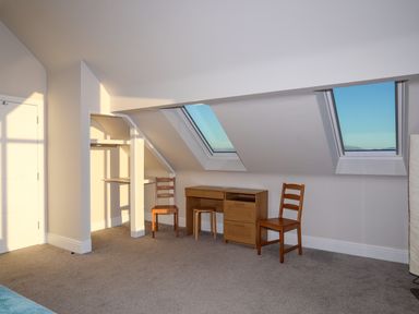 A room with a small wooden desk and two wooden chairs under slanted windows at Plas Gwylan in Rhosneigr