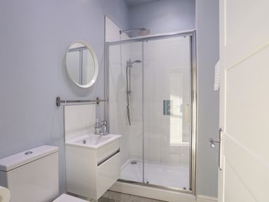 A bathroom with a toilet sink vanity mirror and glass shower enclosure at Plas Gwylan in Rhosneigr