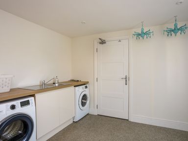 A laundry room with washing machines a sink and two blue hanging drying racks at Plas Gwylan in Rhosneigr