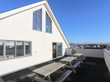 A terrace with three wooden picnic tables outside a white building with large windows at Plas Gwylan in Rhosneigr