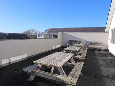 A rooftop terrace with wooden picnic tables and benches surrounded by a low wall at Plas Gwylan in Rhosneigr