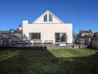 The back of a house with a patio area featuring picnic tables and benches and a grass lawn in front at Plas Gwylan in Rhosneigr