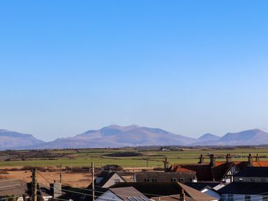 A view of rooftops and fields with mountains in the background at Plas Gwylan in Rhosneigr