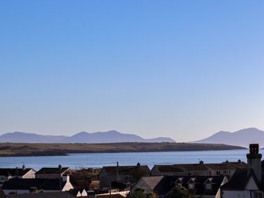 A coastal landscape with rooftops of houses in the foreground and a body of water with hills in the background at Plas Gwylan in Rhosneigr