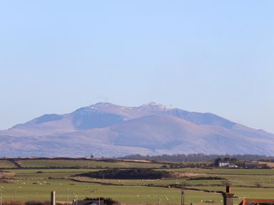 A landscape with green fields and scattered sheep with mountains in the background at Plas Gwylan in Rhosneigr