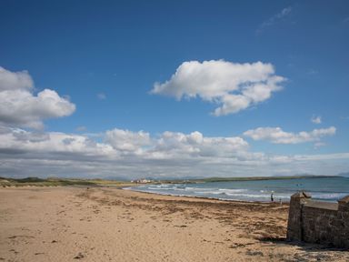 A sandy beach with seaweed and waves under a blue sky with clouds at Plas Gwylan in Rhosneigr