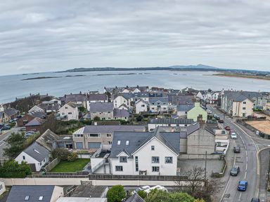 A coastal town with houses streets and parked cars overlooking a body of water at Plas Gwylan in Rhosneigr