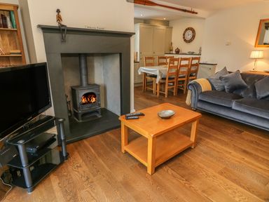 A living room with a wood burning stove television and dining table at Woodbine Cottage in Ambleside