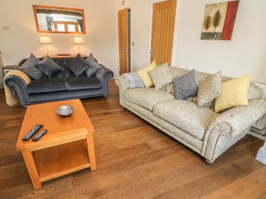 A living room with two sofas a wooden coffee table with remotes and a bowl a wall mirror and a painting at Woodbine Cottage in Ambleside