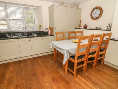A kitchen with wooden floor a dining table with six chairs a sink and cabinets at Woodbine Cottage in Ambleside