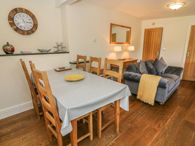 A dining area with wooden table and chairs next to a living room with a sofa and lamps at Woodbine Cottage in Ambleside