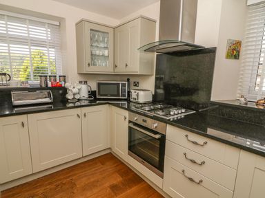 A kitchen with white cabinets black countertops a gas stove oven microwave toaster and windows with blinds at Woodbine Cottage in Ambleside