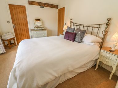 A bedroom with a double bed with pillows bedside tables with lamps a dressing table and wooden doors at Woodbine Cottage Ambleside